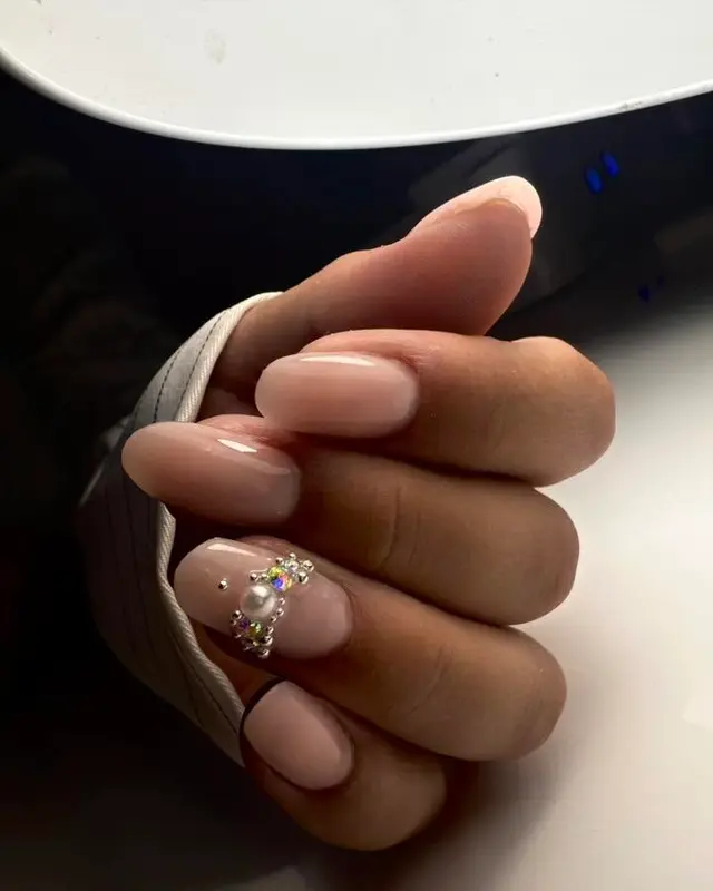 Ongles courts nude au rendu naturel, bijou sur l’annulaire